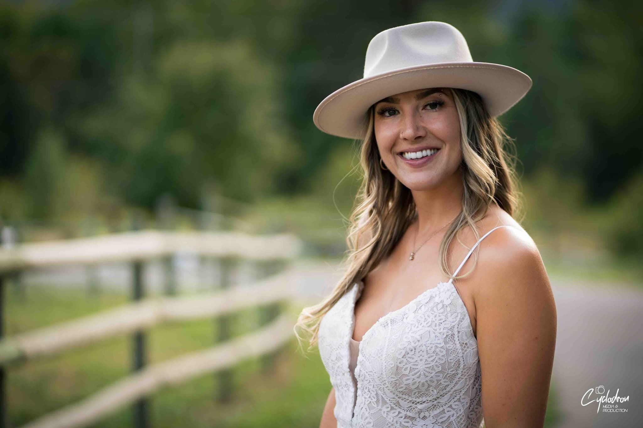 Outdoor portrait of woman in white lace dress and cream fedora hat with natural lighting